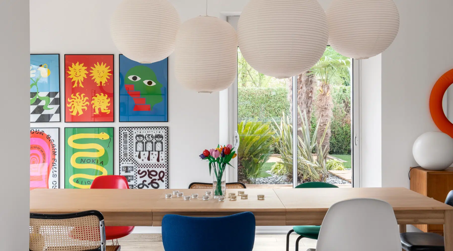 Airbnb déco pop art : salle à manger avec grande table en chêne, suspensions boules blanches et mur d'affiches graphiques, gîte kids friendly Côte d'Émeraude