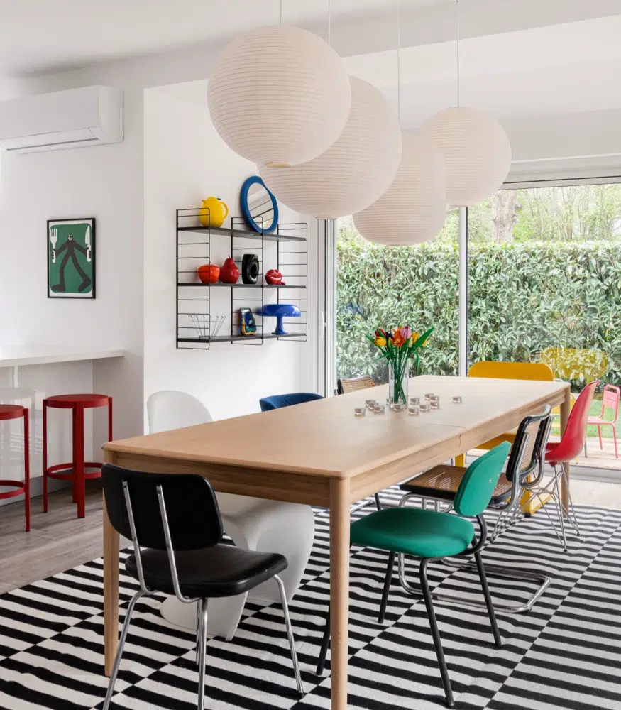 Airbnb déco colorée : séjour avec chaises vintage dépareillées, tapis rayé noir et blanc et affiches pop art, logement saisonnier Bretagne
