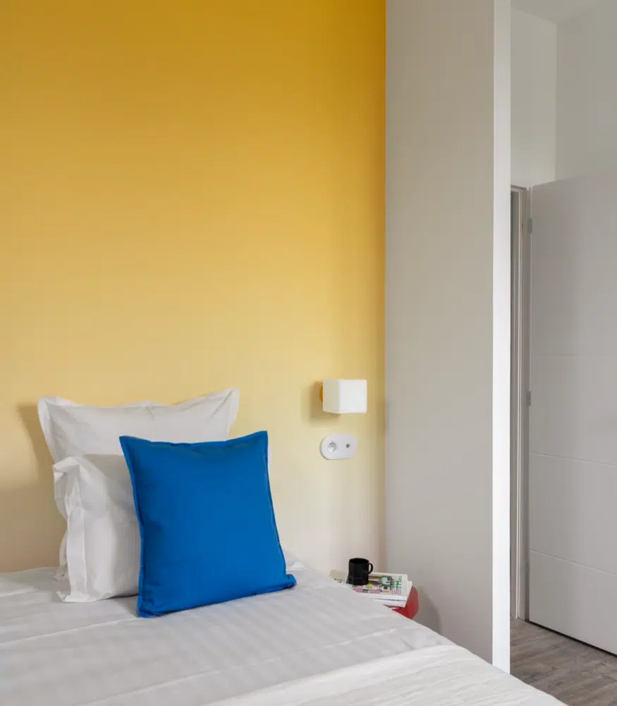 Airbnb déco chambre simple : mur en arche jaune solaire et coussin bleu, logement saisonnier kids friendly Côte d'Émeraude