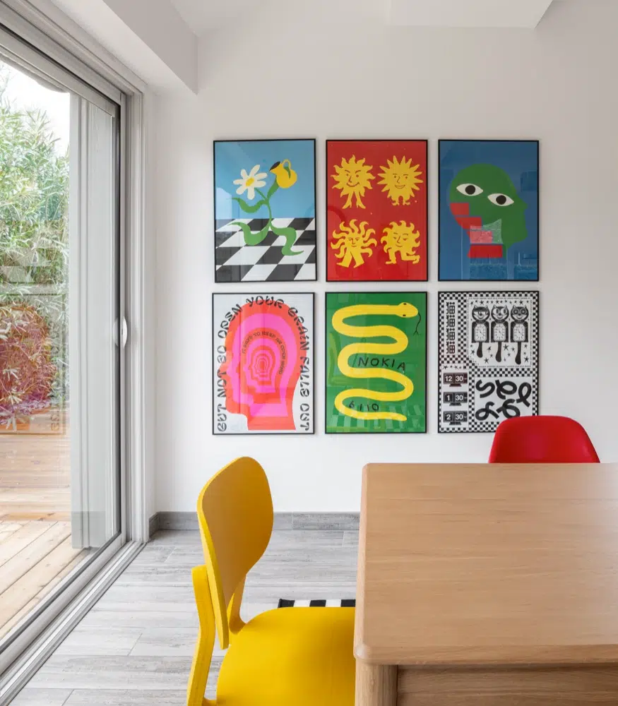 Airbnb déco kids friendly : salle à manger avec chaises multicolores, affiches graphiques et vue sur jardin, projet Le P'tit Bois Saint-Jouan-des-Guérets