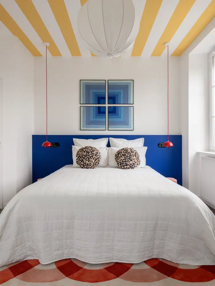 Chambre Airbnb design : tête de lit peinte bleu cobalt, coussins léopard et luminaire FlowerPot rouge